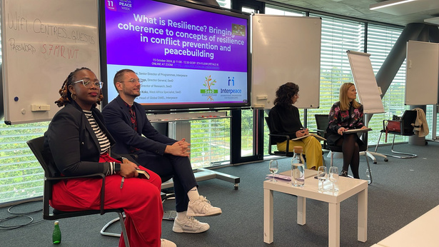 Alexander Guest seated with fellow speakers at a Geneva Peace Week workshop on resilience, with the event title displayed behind the panel.